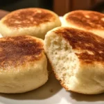 Freshly baked English muffins stacked on a wooden table.