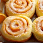 Freshly baked orange sweet rolls with icing on a rustic table