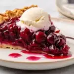 Slice of tart cherry pie topped with whipped cream on a plate