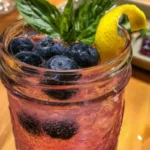 A refreshing Blueberry Gin Fizz cocktail garnished with blueberries and mint.