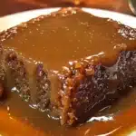 Warm sticky toffee pudding topped with buttery toffee sauce on a plate